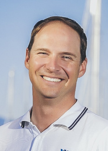 Ein Mann in einem weißen Hemd lächelt hinter der Bühne vor einem Boot.